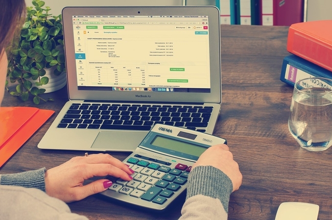 Vivo Regulariza: Foto de uma pessao sentada em frente a uma mesa. Na mesa tem um notebook aberto com a tela ligada numa planilha, uma calculadora e um copo d'água. A pessoa está fazendo contas na calculadora!